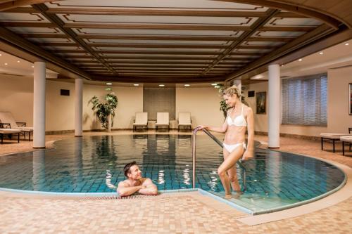 a man and a woman in a swimming pool at Hotel Genziana in Selva di Val Gardena