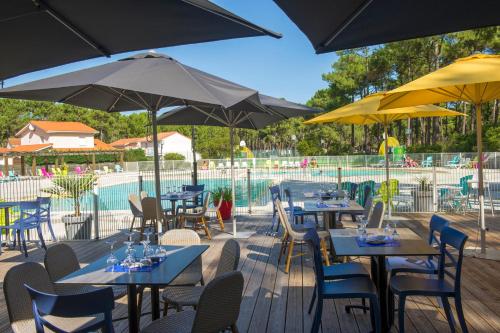 a patio with tables and umbrellas and a pool at VTF La Jaougue Soule in Biscarrosse-Plage