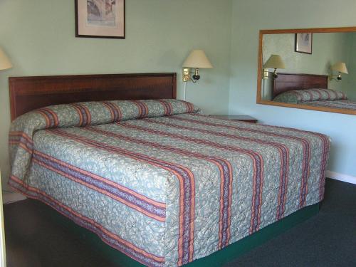 ein großes Bett in einem Hotelzimmer mit Spiegel in der Unterkunft American Inn Motel in Many