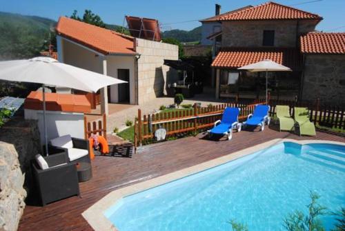 a swimming pool with chairs and umbrellas next to a house at Casa do Parada in Messegães