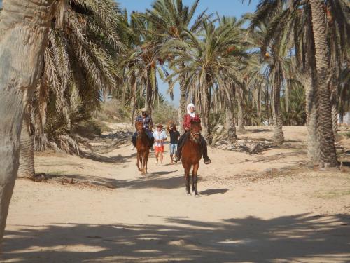 two people riding horses on a beach with palm trees at Menzel Churasco Djerba in Aghīr