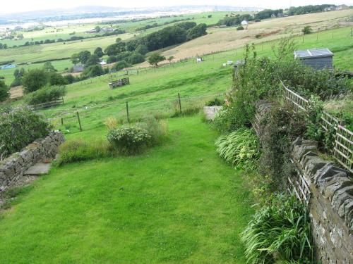a grassy hill with a stone wall and a field at Midsummer Barn in Darwen