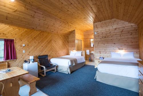 Habitación con 2 camas, escritorio y mesa. en Northern Rockies Lodge, en Muncho Lake