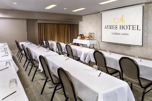 a conference room with white tables and chairs and a screen at Ayres Suites Yorba Linda/Anaheim Hills in Anaheim