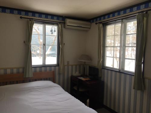 een slaapkamer met een bed en 2 ramen bij Chateau Lausanne in Hakuba