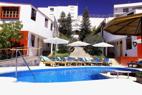 a swimming pool with chairs and umbrellas next to a building at Hotel Villa Jazmin in Ica