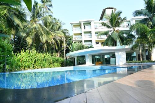 a swimming pool in front of a building with palm trees at B&F Kensington Square in Siolim