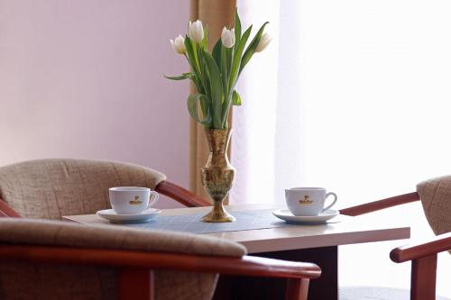 a table with two cups and a vase with flowers at Hotel Aleksander in Ustka