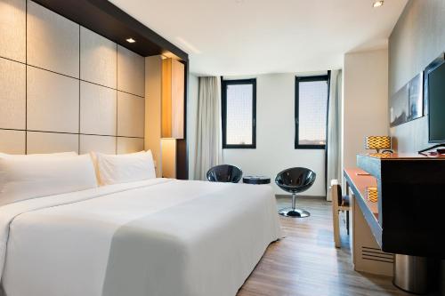 Habitación de hotel con cama blanca grande y escritorio. en Hotel Barcelona Condal Mar Affiliated by Meliá, en Barcelona