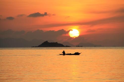 a man in a boat in the ocean at sunset at Nice Sea Resort in Srithanu