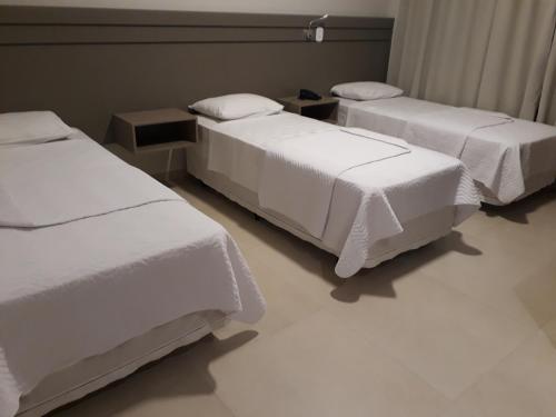 a room with three beds with white sheets at Pak Suítes Hotel in Luis Eduardo Magalhaes
