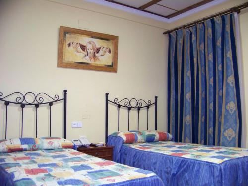 2 camas en una habitación con cortinas azules en Hostal Restaurante El Lirio en Bollullos par del Condado