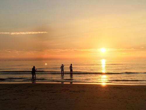 three people standing on the beach at sunset at Hotel Meyer in Bergen aan Zee
