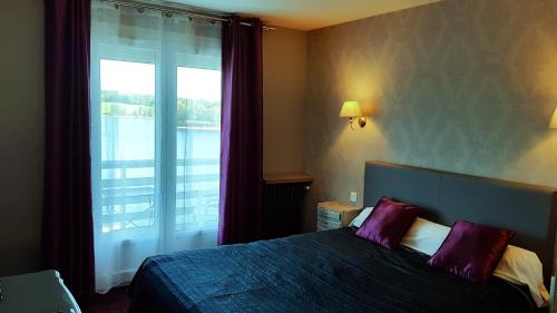 a bedroom with a bed with purple pillows and a window at Hotel Restaurant La Caravelle in Peyrat-le-Château
