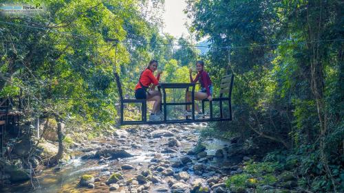 two women sitting on a suspension bridge over a river at Namkat Yorla Pa Resort in Ban Kat