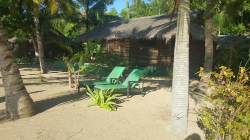 two green chairs sitting in front of a hut at Anjiamarango Beach Resort in Nosy Be