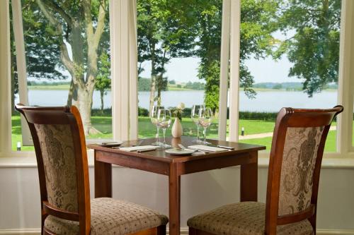 a table and two chairs with wine glasses in front of a window at Normanton Park Hotel, Sure Hotel Collection by Best Western in Oakham