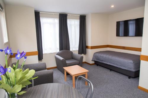 a hotel room with a bed and chairs and a tv at Dunedin Motel and Villas in Dunedin