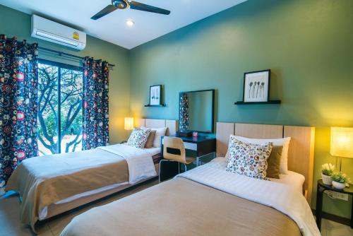 a bedroom with two beds and a desk and a window at Villa Na Pran, Pool Villa in Pran Buri