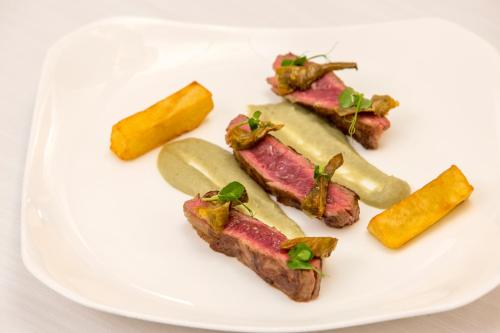 a white plate with meat and vegetables on it at Hotel Hermitage Relais & Châteaux in Breuil-Cervinia