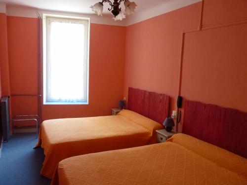 2 camas en una habitación con paredes de color naranja y ventana en Hotel Régina, en Salon-de-Provence