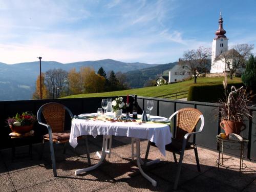 a table with wine glasses on a balcony with a church at Berg-Arche in Sankt Margarethen im Lavanttal