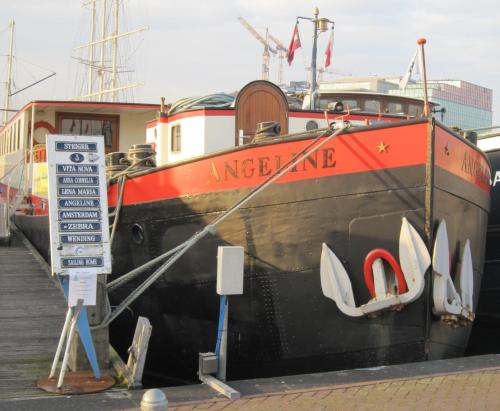 un bateau orange et noir garé sur un quai dans l'établissement Hotelboat Angeline, à Amsterdam