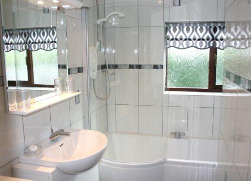 a white bathroom with a sink and a bath tub at Emerald Bank Cottage in Uldale