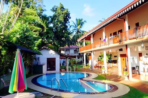 a swimming pool in front of a hotel with an umbrella at Haus Berlin in Bentota