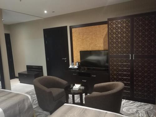 a hotel room with a bed and a tv and chairs at Naviti Warwick Al Khobar in Al Khobar