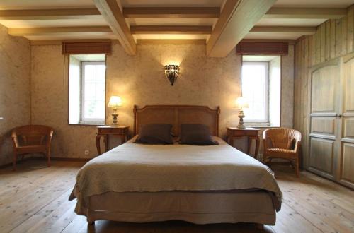 a bedroom with a bed with two chairs and two windows at Gites Du Manoir de Savigny in Valognes
