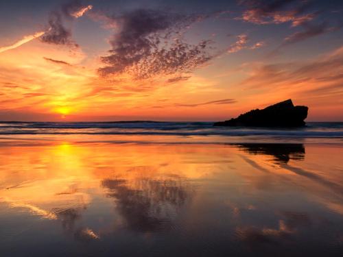 a sunset on the beach with a rock in the water at Pontalaia Apartamentos Turísticos in Sagres