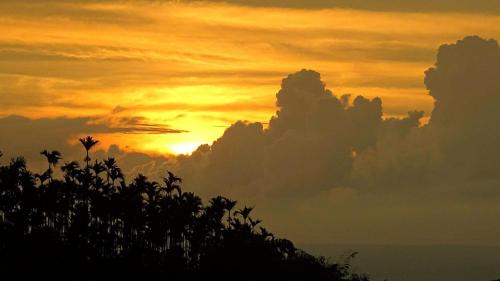 a sunset with clouds and trees in the foreground at 幸福檜木屋民宿 in Gukeng