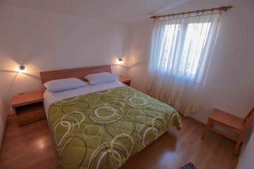 a bedroom with a bed with a green blanket and a window at Apartments Mama in Rogoznica