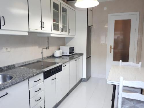 a kitchen with white cabinets and a sink and a table at Piso Camino de Santiago 2 in Sarria