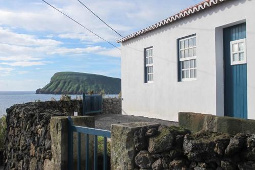 a white house with a stone wall next to the ocean at Canário do Mar - Rural Tourism in Angra do Heroísmo