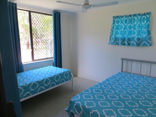 a bedroom with a bed and a window with blue sheets at Fraser Forever Orchid Beach Fraser Island in Fraser Island