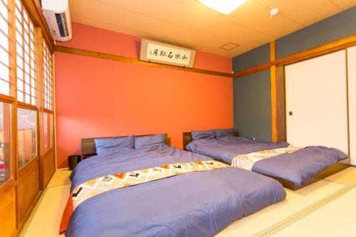 2 camas en una habitación con pared de color naranja en Guest House Kyorakuya Kinkakuji en Kyoto