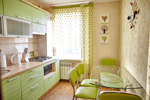 ヴィーンヌィツャにあるFamily apartment on Shevchenko streetのキッチン(緑のキャビネット、ガラスのテーブルと椅子付)