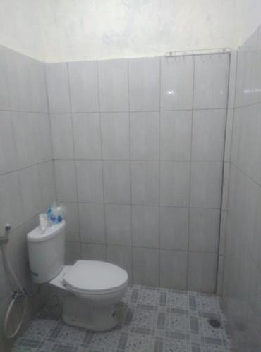 a bathroom with a toilet in a white tiled room at Pedek Homestay in Praya