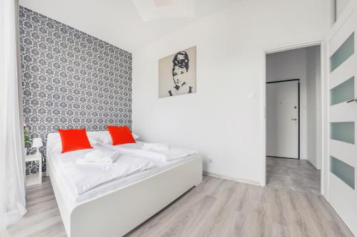 Apartamenty Sun & Snow Mila Baltica في غدانسك: غرفة بيضاء مع سرير مع وسائد برتقالية