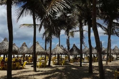 una playa con sombrillas, sillas de paja y palmeras en Residence Van Piaget, en Fortaleza