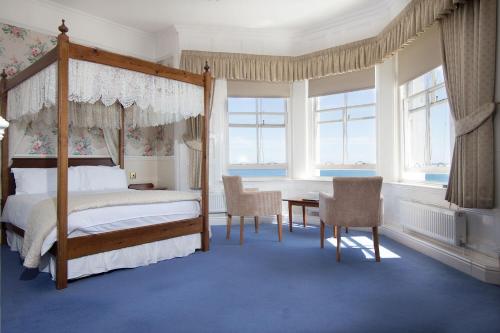 um quarto com uma cama de dossel, uma mesa e cadeiras em The Queens Hotel em Penzance