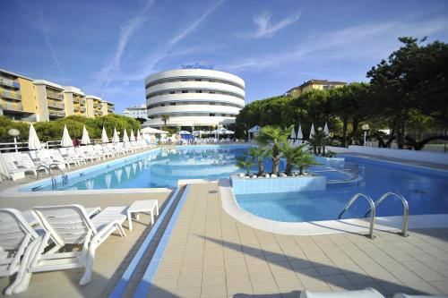 une piscine avec des chaises blanches et un bâtiment dans l'établissement Hotel Corallo, à Bibione