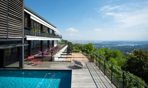 un bâtiment avec une piscine et des chaises sur un balcon dans l'établissement L'Ermitage Hôtel Cuisine-À-Manger, à Saint-Cyr-au-Mont-dʼOr