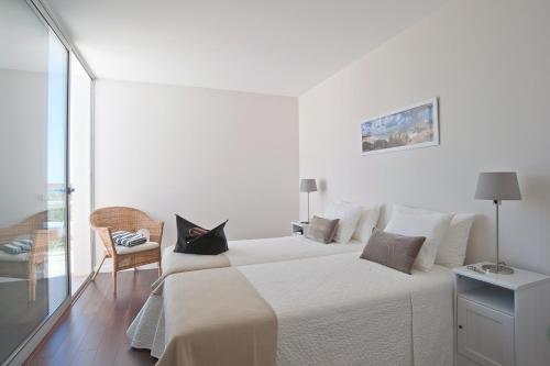 a white bedroom with a large bed and a chair at Seasagres - Design Villas in Sagres