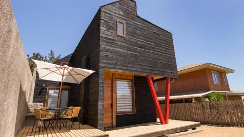 a small black house with a table and an umbrella at Comarca Lodge in Pichilemu