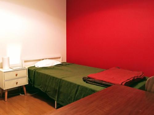 a bedroom with a green bed and a red wall at Guesthouse LuLuLu 無料朝食&夕食ｶﾚｰ 街まで電車8分 ﾛｰｿﾝ隣 in Kochi