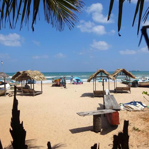 a beach with a bench and umbrellas and the ocean at Hotel Angel Inn Beach in Trincomalee