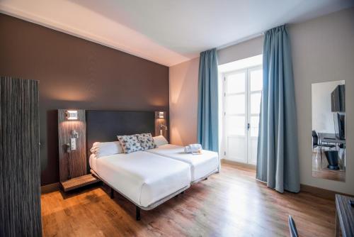sypialnia z dużym białym łóżkiem z niebieskimi zasłonami w obiekcie Petit Palace Santa Cruz w Sewilli